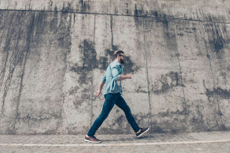 Young stylish bearded man is rushing to the meeting. He is in a casual outfit, with glasses, walking outsideの写真素材