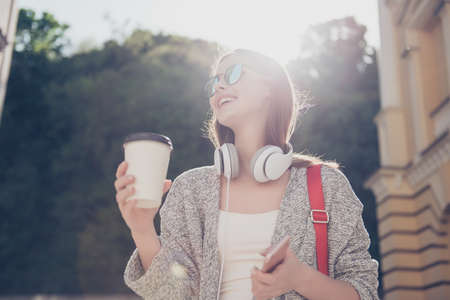 Sunny mood. Young cheerful smiling girl in sunglasses at the vacation. She is happy, wearing casual clothes, drinks coffeeの写真素材