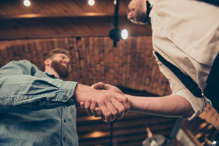 Low angle view of a hanshake of the red bearded client and classy dressed stylist of a barber shop in a loft styleの写真素材