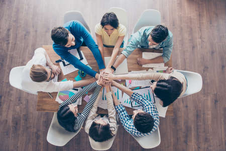 Top view of business people putting their hands on top of each other in nice light workstation,...