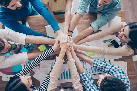 Cropped top view of business people putting their hands on top of each other in nice light workstation, wearing casual clothes. Conception of successful team buildingの写真素材