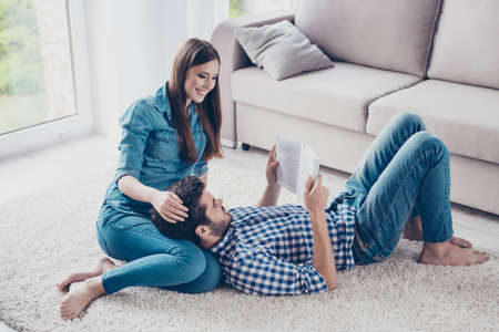 Happy beautiful couple is spending weekend together on the floor on carpet at home, relaxing and enjoying the company of each other, he is lying on her kneesの写真素材