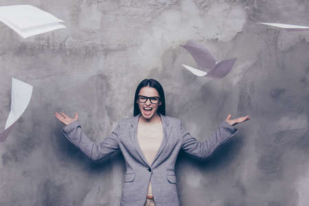 Angry woman in is screaming and tossing the papers on the grey background