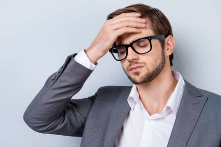 Close up portrait of tired sick handsome young man touching his forehead. He is wearing the...
