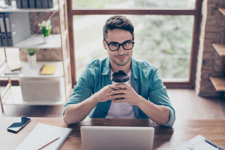 Close up photo of smiling happy man in casual clothes holding a cup of tea and dreaming about weekendの写真素材