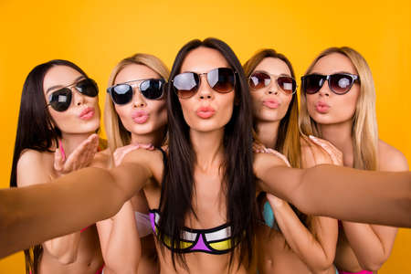 Selfie time, girls! Five girlfriends in fashionable different swim suits and sunglasses are posing for a selfie photo, that brunette is taking. They are all sending air kiss, making memoriesの写真素材