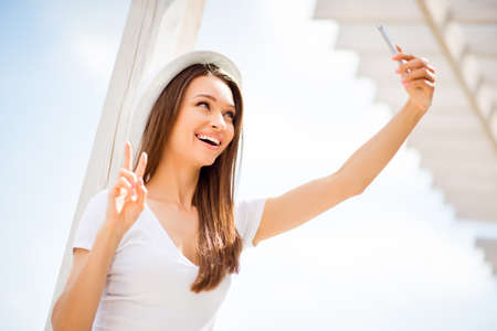Carefree and happy, funky mood. Low angle of cute young girl, making selfie on a camera of her pda...