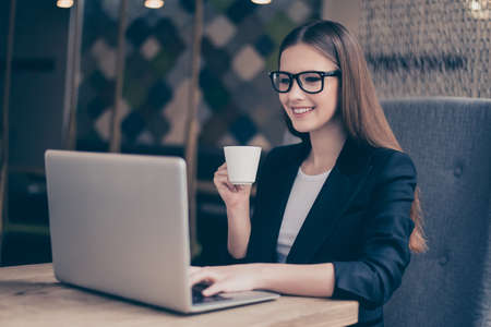 Lunch time. Successful relaxed dreamy business lady lawyer is resting at her work place in a cafe and drinks coffee , looking in the screen of laptopの写真素材