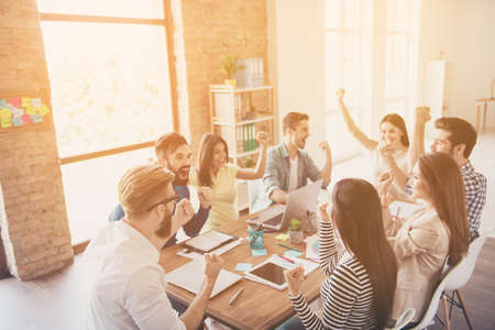 Close up of successful team of business partners with raised up hands in light modern workstation, celebrating the growth of the incomeの写真素材