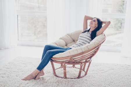 Young pretty smiling lady sitting on the armchair having a rest and dreaming with closed eyesの写真素材