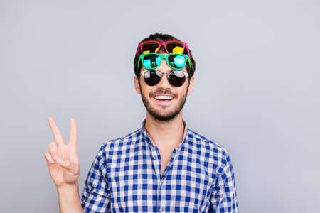 Playful young brunette bearded man in three pairs of bright colorful glasses and checkered casual...