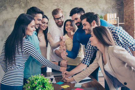 business people putting their fists on top of each other on the desktop in nice light workstation, wearing casual clothes.の写真素材