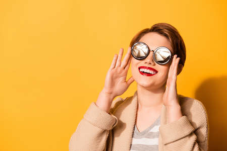 Stunning look of a cute girl with adorable smile wearing stylish sunglasses and casual clothes on the bright yellow backgroundの写真素材