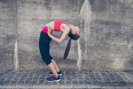 Young fashionable sportswoman is stretching on the street on a summer day. She is very bendy and flexible, doing nice yoga position, wearing trendy sport outfit, shoesの写真素材