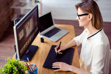 Young professional retoucher sitting at the table at home and working with graphic digital tablet