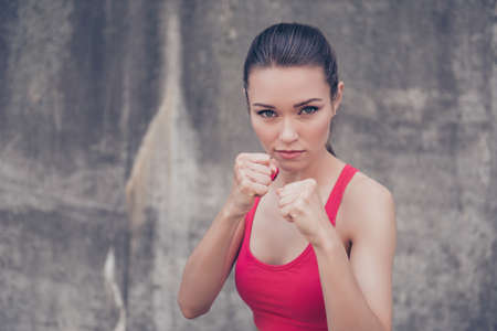 Close up portrait of attractive serious fit boxer, ready for fight, on concrete wall background, wearing pink fashionable sport wearの写真素材