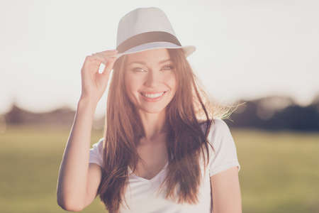 Young gorgeous brunette girl on vacation, in a stylish hat, casual outfit, holding her cap, so dreamy and charming, smilingの写真素材