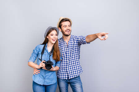 Happy young couple of tourists are on vacation, in casual outfits, hats and with camera, isolated on pure backgroundの写真素材