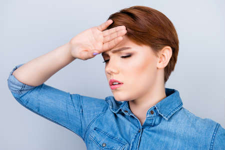 Close up portrait of ill young woman measuring the temperature of her body by touching forehead at...