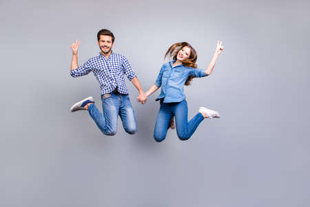 Cheerful and playful couple in casual outfits are jumping and gesturing peace signs indoors, smiling, posingの写真素材