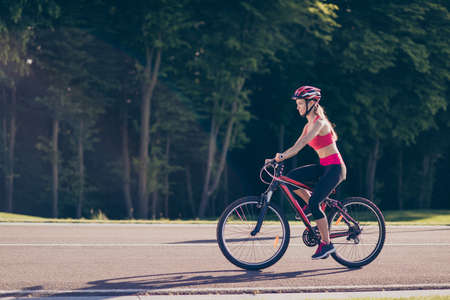 Young girl is on a bike outdoors in nice spring park, wearing helmet and trendy sport outfit, sneakers, smilingの写真素材