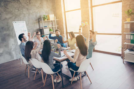 Successful business team with raised up hands in light modern workstation, celebrating the breakthrough in their companyの写真素材