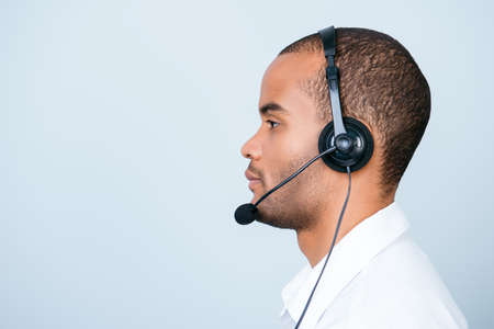 Side profile portrait of a handsome mulatto american guy call centre operator in a headset. He is isolated on a pure light background, wearing formal wearの写真素材