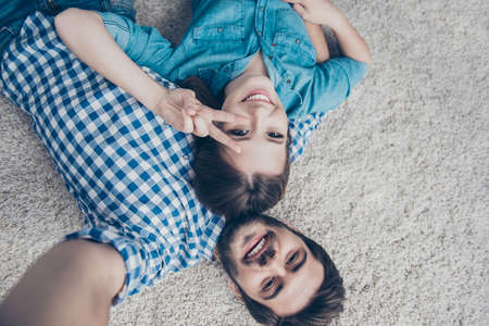 Upside down shot of a couple of teens. Young siblings are lying at home on the carpet and take a selfie in casual outfit, smiling and posingの写真素材