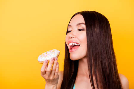 Diet and calories concept. Close up cropped portrait of happy asian girl  eating donut, so hungry...