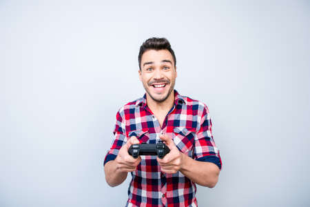 Single man`s life. Cheerful young brunet guy is playing games indoors, enjoying himself, wearing casual outfit, on a light blue backgroundの写真素材