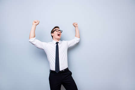 yes successful young handsome student is celebrating. he is in a formal outfit and black stylish glasses, on pure background, with  hands raised upの写真素材