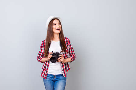 Young cheerful brunette female tourist photographer is smiling on the light blue background. She is excited and holding camera, wearing hatの写真素材