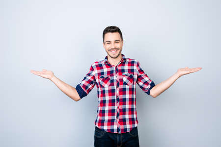 Cheerful brunet student in casual wear on pure background is gesturing with hands like he is holding something and need to choose between two optionsの写真素材