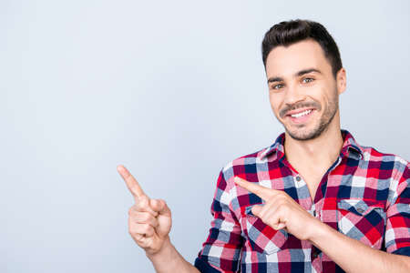 Young cheerful successful entrepreneur on the pure light blue background is smiling, wearing casual outfit and is pointing on a copyspace with his fingersの写真素材