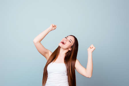 A dream of the young cute brunette lady came true. She is very excited, wearing summer outfit, celebrating with raised hands, on a light blue backgroundの写真素材