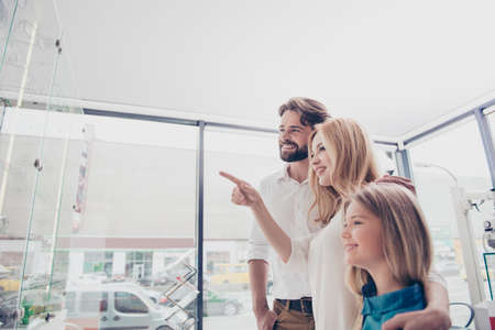 Consumering and family  concept. Three happy relatives are choosing glasses in an eye clinic`s boutique, blond cute mom is showing the one she liked, all smilingの写真素材