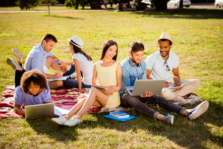 Classmate, international friendship, summer, communication, education and teenage concept. Friendly students teenagers with books and devices are studying outdoors together, lying on the groundの写真素材