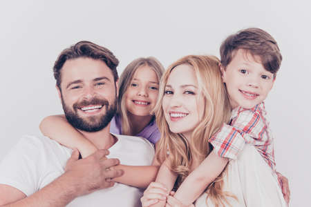 Family photo portrait. Four relatives are hugging on the white background, smiling, at home, blond mum is piggy backing the cute small sonの写真素材