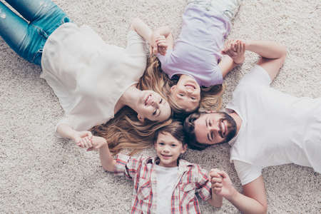 Top view of four relatives, lying on the beige cozy carpet at home, holding hands, all smiling, wearing casual outfitsの写真素材