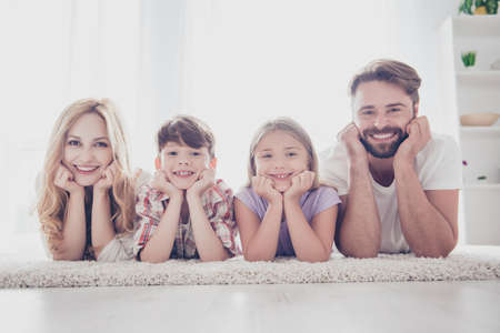 Happy family concept. Four relatives are lying on the carpet on the floor, holding heads with arms,...