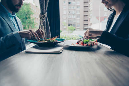 Low angle of two young business partners are sitting in a fancy restaurant, wearing smart outfits and eating delicious salads, smiling, enjoyingの写真素材