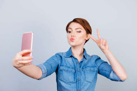 Cheerful woman showing v-sign while  taking selfie on her smartphone