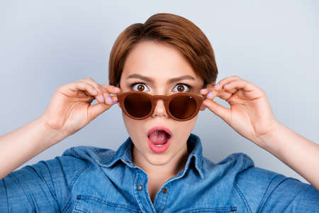 Close up portrait of shocked and amazed pretty young girl touching sunglassesの写真素材