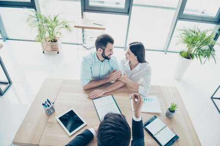 High angle top view of cheerful married couple, getting a car key from a car dealer in the showroom and signing contract, they are dressed in formal outfits, smilingの写真素材