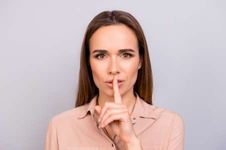 Shh! Keep my secret. Attractive young brunette woman in beige formal shirt is showing someone to...