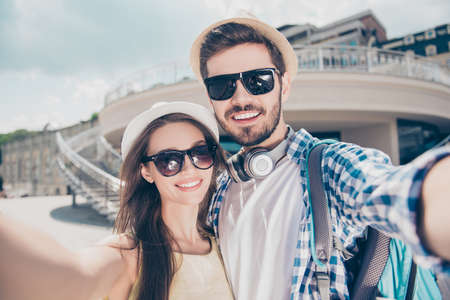 Close up of a cheerful young couple making selfie photo on camera. They are in tourist`s outfits,...