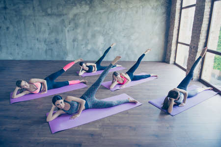 Five concentrated cute fit young ladies, stretching their legs by doing exercise, wearing fashionable sport wear, barefoot on a purple carpets in loft modern studioの写真素材