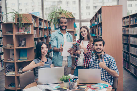 We like education! Successful future for smart youth! Four attractive young bachelors are welcoming in their university`s library, gesturing thumbups, smiling, wearing casual smartの写真素材