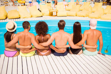 Back view of three hot ladies with perfect figures, boyfriends embracing them, hugging waists, sitting near pool.の写真素材