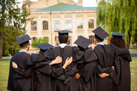 Back view of six successful graduates in black robes, bonding, in mortar-boards with red tassels, black gowns. They did it, passed exams, finished course of studies, got the master degree togetherの写真素材